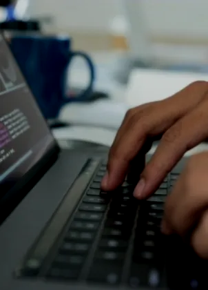 Hands working on a laptop beside source code