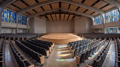 a large church hall with a wooden stage and rows of empty seats under stained glass windows